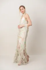 Vestido largo de gasa con escote halter, volado central y falda con flecos, acompañado de foulard. Diseño estampado en tonos claros con detalles sutiles.
