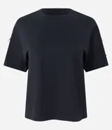 Camiseta blanca de algodón con cuello redondo y mangas cortas, decorada con pequeños lazos brillantes en los laterales de las mangas.
