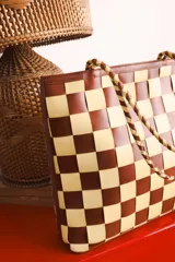 Bolso tipo tote de cuero trenzado a mano con diseño de damero en colores marrón y beige. Cuenta con doble asa trenzada y forro interior.