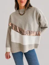 Buzo de tejido de punto con diseño oversize y calce relajado. Presenta un diseño de bloques de color en tonos neutros con una franja diagonal central en material metalizado brillante. Cuenta con cuello redondo y mangas largas con puños acanalados.