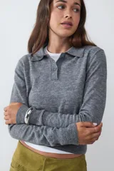 Suéter tejido de punto color gris, con cuello polo y escote en V con un botón. Tiene mangas largas y está confeccionado en un tejido suave y liviano.