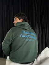 Canguro verde oliva con capucha y cordones ajustables. Estampado en la espalda con la frase "Bad Ideas Good Stories" en letras azules.