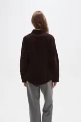 Camisa de pana color marrón, con cuello camisero, cierre frontal de botones y bolsillos en el pecho. Presenta un corte entallado y mangas largas.