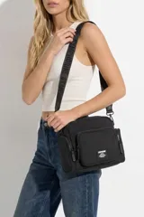 Bandolera negra de nylon con múltiples bolsillos con cierre en el frente y los laterales, y correa ajustable con inscripciones de la marca.