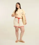 Blusa de corte boxy color beige con rayas finas horizontales, cuello redondo y mangas cortas con dobladillo. Presenta un delicado bordado de cajú en el pecho.