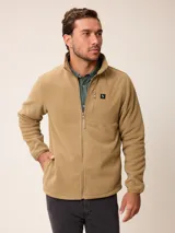 Campera de polar color beige con cierre frontal completo y cuello alto. Presenta un bolsillo en el pecho con cierre y detalle de parche con logo. El diseño combina paneles de tejido polar con detalles en tejido técnico en la zona del pecho.