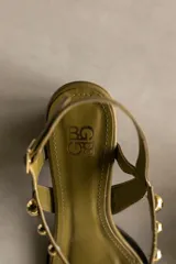 Sandalia de cuero color bronce metalizado, con punta cuadrada, taco ancho y bajo, y tiras finas adornadas con tachas esféricas plateadas.