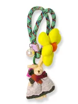 Llavero de mano con cordón trenzado multicolor, decorado con una flor de tela amarilla de gran tamaño, una perla blanca y un dije de peluche con forma de conejo vestido con falda de encaje y cuadros.