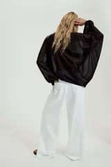 Top de crepe blanco con estampado de lunares negros, escote en V y cierre frontal con finas lazadas. Presenta mangas largas abullonadas con puños elásticos y bajo redondeado.