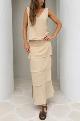 Falda larga color beige de lino tusor, con diseño de recortes en capas con detalles desflecados, de calce relajado y caída natural.