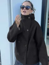 Chaqueta de paño color marrón oscuro, con diseño de doble botonadura frontal y cuello alto estructurado. Presenta mangas largas y un corte recto y holgado.