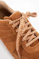 Zapatilla de perfil bajo confeccionada en gamuza color camel, con cordones jaspeados en tonos tierra y suela de goma dentada.