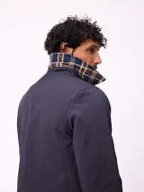 Gabardina de corte clásico en color beige, con cierre frontal de cremallera y botones, cuello camisero y puños ajustables con trabillas.