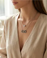 Collar doble de plata 925, compuesto por una cadena superior con dije de punto de luz y una cadena inferior con dije en forma de símbolo de infinito decorado con circonias turquesas.