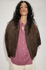 Chaqueta de efecto ante color marrón claro, con cuello solapa, manga larga con trabillas en los hombros y bajo abullonado. Cierre frontal con cremallera y botones ocultos por solapa.
