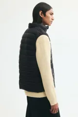 Chaleco acolchado negro de nylon con diseño guateado, cuello elevado, cierre frontal con protección para el mentón y bolsillos laterales. Corte entallado y diseño repelente al agua.