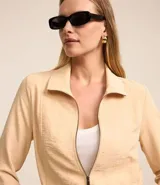 Campera bomber femenina color beige claro, confeccionada en tejido Airflow texturado. Presenta cuello solapa, cierre frontal de cremallera y puños y bajo elásticos.