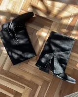 Bota de caña media color negro, de cuero vacuno, con botamanga y tachas plateadas.