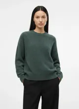 Sweater de punto grueso en color verde oscuro melange, con cuello redondo, hombros caídos y terminaciones acanaladas en puños y ruedo.