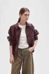 Chaqueta de eco-cuero en color bordó con acabado brillante, diseño holgado, cuello camisero, cierre frontal con botones a presión y detalle de elástico fruncido en el ruedo.