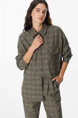 Camisa de corte holgado con cuello clásico, cierre frontal de botones y bolsillo en el pecho. Presenta un diseño de estampado a cuadros en tonos marrones y azules.