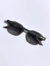 Lentes de sol con armazón de marco completo en color gris mate, con detalles decorativos en color rojo en las esquinas y patillas. Cuentan con cristales oscuros polarizados con protección UV 400.