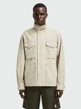 Chaqueta Moncler de estilo utilitario en color beige, con cuello alto, cierre frontal con botones a presión y múltiples bolsillos delanteros.