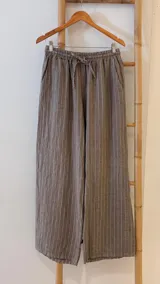 Pantalón de corte ancho y relajado, confeccionado en lino con diseño de rayas verticales. Presenta cintura elástica con cordón de ajuste y bolsillos laterales.