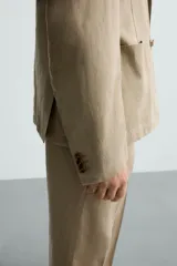 Blazer color beige de corte relaxed fit, confeccionada en tejido con viscosa. Tiene cuello con solapas de muesca, manga larga con puño abotonado, bolsillos frontales de plastrón, medio forro interior, aberturas en la espalda y cierre frontal con botones. Presenta un efecto lavado.