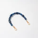 Correa decorativa para cartera compuesta por cuentas de resina en tonos azules con efecto marmoleado y ganchos metálicos dorados en los extremos.