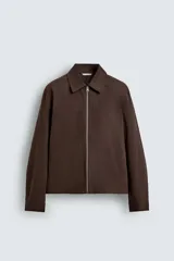 Sobrecamisa de corte regular confeccionada en tejido con estructura canvas color marrón. Presenta un ligero acolchado interior, cuello de solapa y cierre frontal con cremallera metálica. Incluye dos bolsillos de plastrón en el pecho y bolsillos laterales de vivo, con mangas largas terminadas en puños con botón.