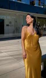 Vestido largo tipo slip dress de satén dorado, con escote en V, breteles finos y corte al bies que se ajusta suavemente a la figura.