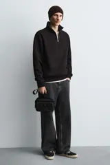 Bandolera negra de acabado engomado con compartimento principal con cierre de cremallera y bolsillo interior plano. Bolsillo frontal con cierre de cremallera. Asa de hombro ajustable y extraíble.