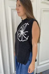 Chaleco de lana color crema con diseño de flor bordada en relieve en el frente, cuello redondo y aberturas laterales en el ruedo.