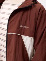 Rompevientos Rusty con capucha, diseño bicolor en azul marino y gris, cierre frontal y logo bordado en el pecho.