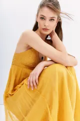 Vestido largo color mostaza con escote en V y breteles finos cruzados en la espalda. El corpiño está adornado con canutillos bordados, y la falda es fluida.