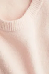 Buzo de punto fino color rosa pálido, con cuello redondo y mangas cortas. Presenta remates acanalados en el cuello, puños y bajo.