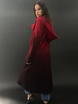 Tapado rojo con capucha, confeccionado en lana merino teñida con técnica tie-dye. Tiene corte recto, largo, bolsillos laterales y cierre cruzado con broches a presión ocultos.