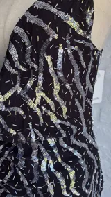 Vestido corto negro con lentejuelas plateadas dispuestas en un patrón ondulado o geométrico. Presenta un escote profundo en V pronunciado y tirantes finos tipo espagueti.