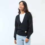 Sweater de punto negro con diseño cruzado tipo cárdigan, escote en V profundo y cierre lateral con un botón decorativo grande de efecto carey. Presenta mangas largas con puños ajustados.