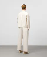 Camisa de mujer color crudo, de corte recto, con cuello chimenea abotonado y manga larga con abertura. Presenta botonadura frontal y bolsillos de plastrón con logo bordado en el pecho.