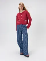 Cardigan de algodón grueso color rojo, con cuello redondo, cierre frontal de botones grandes y bolsillos cuadrados en el frente. Presenta detalles de pelo sintético en el cuello y los bolsillos, y logo bordado en uno de los bolsillos.