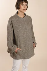 Capa de lana fina sin teñir, con estampado de espiga en tonos marrones y beige. Presenta cuello alto, mangas amplias, bolsillos laterales y pinzas en la parte delantera.