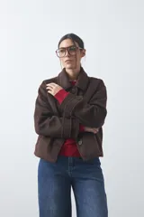 Tapado corto de paño con textura, color marrón, de corte recto y silueta estructurada. Presenta cuello camisero, cierre frontal con botones grandes y mangas largas con detalle de trabas en los puños.