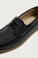 Zapato náutico de piel color beige, con cordones y ojalillos metálicos, suela plana de goma marrón y costuras visibles en la puntera.