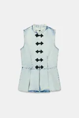 Chaleco de denim claro con efecto lavado, cuello mao, sin mangas y corte peplum con pliegues en la parte inferior. Cierre frontal con botones de alamares negros.