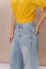 Pantalón de jean estilo barrel con tiro alto y pierna amplia de diseño curvo. Presenta un lavado celeste claro con efecto desgastado, cierre y botón frontal, y bolsillos funcionales.