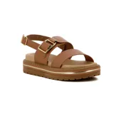 Sandalia de plataforma color caramelo con dos tiras anchas sobre el empeine, una de ellas con una hebilla grande y rectangular de metal dorado. La suela es gruesa y dentada, con detalles de líneas doradas en el lateral.