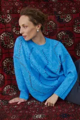Buzo de punto color beige con diseño de trenzas y costuras decorativas en contraste que forman rombos. Presenta cuello redondo, mangas largas y puños acanalados.