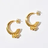 Aros de bronce bañados en oro con forma de medialuna y detalle de tres dijes colgantes con forma de esfera. Cierre de tuerca a presión.